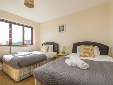 A bedroom with two single beds each with grey bedspreads and patterned pillows and a nightstand with a lamp between the beds at Surfside in Marazion