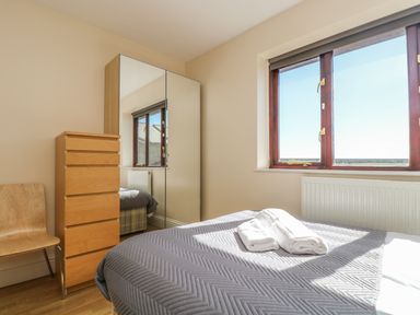 A bedroom with a bed covered in a gray blanket and two folded white towels on top a wooden chair a wooden chest of drawers and a mirror wardrobe near a window at Surfside in Marazion