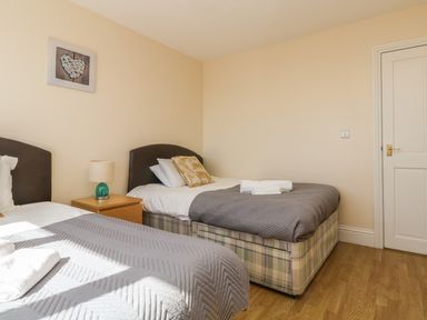 A bedroom with two single beds a nightstand with lamp and a door at Surfside in Marazion