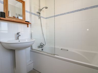 A bathroom with a sink pedestal, a bathtub with a showerhead, and a wooden framed mirror at Surfside in Marazion