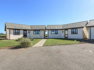 Two single-story houses with tiled roofs and grass lawns connected by a paved path at Surfside in Marazion