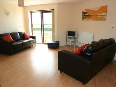 A living room with two black sofas with red cushions a small TV on a glass stand and a sliding glass door leading outside at Sea Shore in Marazion