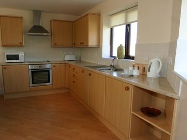 A kitchen with wooden cabinets an oven microwave toaster kettle sink and a window at Sea Shore in Marazion