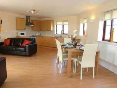 An open plan living room and kitchen with a black sofa and a dining table with chairs at Sea Shore in Marazion