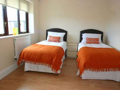 A bedroom with two single beds orange throws and pillows between a window and a nightstand at Sea Shore in Marazion