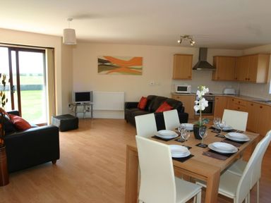 An open plan living and kitchen area with dining table set for six and two black sofas at Sea Shore in Marazion
