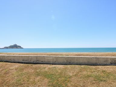 A grassy area with a low concrete wall overlooking the sea and a small island in the distance at Sea Shore in Marazion