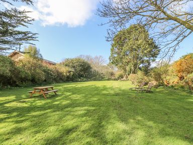 An outdoor garden area with grass a wooden picnic bench and two wooden lounge chairs at Boskednan Wartha in Penzance