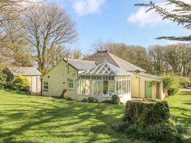 A house with a glass conservatory surrounded by trees and grass at Boskednan Wartha in Penzance