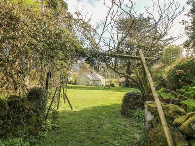 A garden with a metal gate opening to a lawn and a house in the background at Boskednan Wartha in Penzance