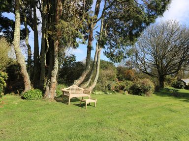 A garden with grass trees a bench and a small table at Boskednan Wartha in Penzance