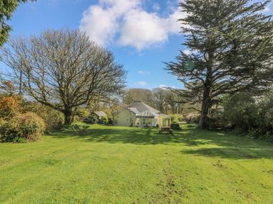 A garden with a lawn chairs and a picnic table in front of a house surrounded by trees at Boskednan Wartha in Penzance