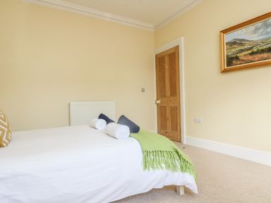 A bedroom with a bed covered in white linens a green blanket and rolled towels a wooden door and a painting on the wall at Boskednan Wartha in Penzance