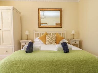 A bedroom with a bed with yellow pillows and a green bedspread and two bedside tables with lamps at Boskednan Wartha in Penzance