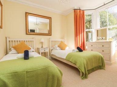 A bedroom with two single beds green blankets and a window with orange curtains at Boskednan Wartha in Penzance