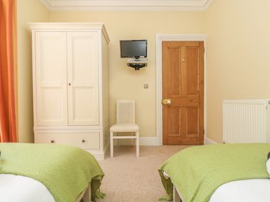 A bedroom with two beds green blankets a wardrobe a chair a wooden door and a wall-mounted television at Boskednan Wartha in Penzance