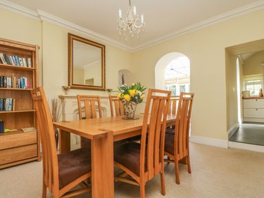 A dining room with wooden table and chairs a bookshelf and a mirror above the fireplace at Boskednan Wartha in Penzance