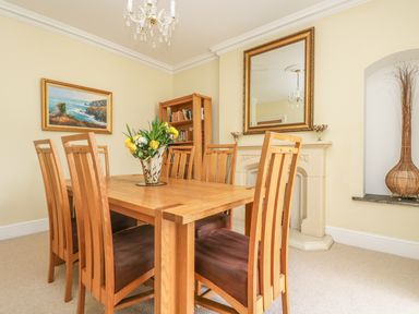 A dining room with wooden table and chairs flowers on the table bookshelf and mirror above a fireplace at Boskednan Wartha in Penzance
