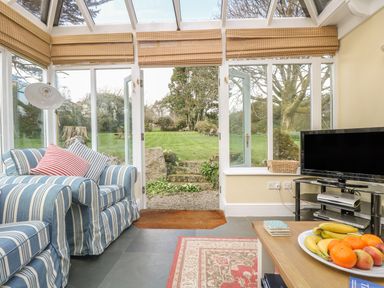 A conservatory with striped sofas a fruit plate on a table and a television at Boskednan Wartha in Penzance