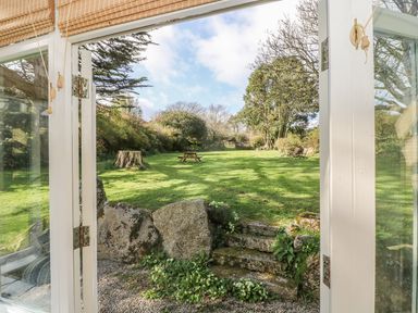 A garden view from a white framed glass door with stone steps and green grass with trees at Boskednan Wartha in Penzance