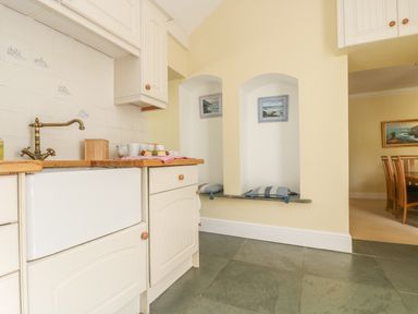 A kitchen area with white cabinets a sink and two small alcoves with cushions and framed pictures at Boskednan Wartha in Penzance