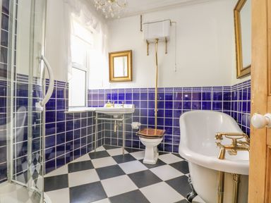 A bathroom with a clawfoot bathtub shower cabin toilet and sink with blue tiled walls and checkered floor at Boskednan Wartha in Penzance