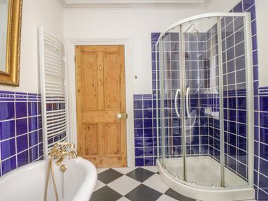 A bathroom with a bathtub a shower enclosure blue tiled walls and a wooden door at Boskednan Wartha in Penzance