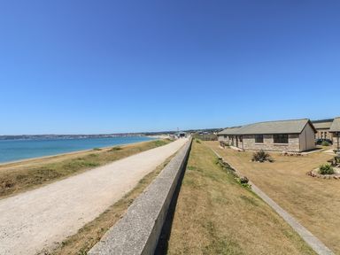 A coastal path next to a stone wall with cottages on grassy land by the sea at Seashells in Marazion