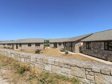 Stone bungalows with picnic tables on grass behind a stone wall at Seashells in Marazion