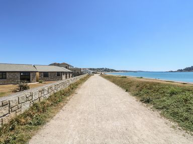 A gravel path along the coast with buildings and a stone wall on the left and the sea on the right at Seashells in Marazion