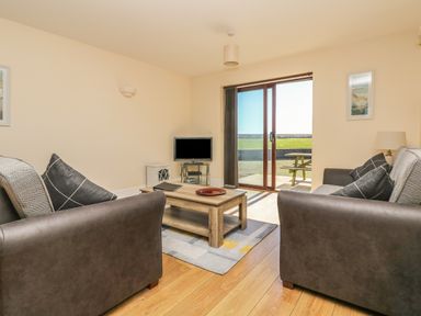 A living room with two sofas a wooden coffee table a television and sliding glass door leading outside at Seashells in Marazion