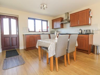 A kitchen with wooden cabinets a dining table with four chairs and a wooden door at Seashells in Marazion