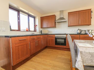 A kitchen with wooden cabinets a countertop a stove a kettle and a dining table at Seashells in Marazion
