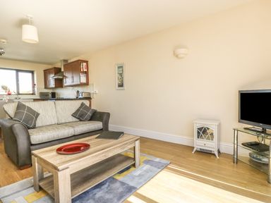 A living room with a sofa coffee table and television with a kitchen in the background at Seashells in Marazion