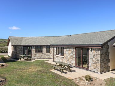 A stone exterior single-story building with two picnic benches on paved areas and grass surrounding at Seashells in Marazion