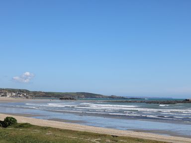 A beach with waves and a shoreline with grass and buildings in the distance at Seashells in Marazion