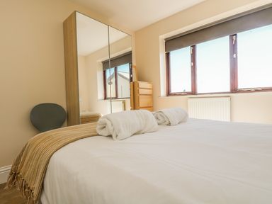 A bedroom with a bed covered in white linens and two rolled white towels reflected in a mirrored wardrobe at Seashells in Marazion
