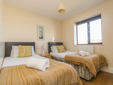 A bedroom with two single beds with brown throws and white towels by a window at Seashells in Marazion