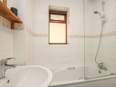 A bathroom with a sink and a bathtub with a showerhead and a small window at Seashells in Marazion