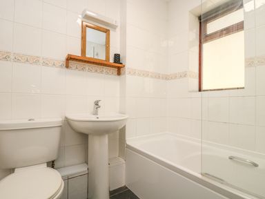 A bathroom with a toilet a pedestal sink a bathtub with a glass screen and a window at Seashells in Marazion