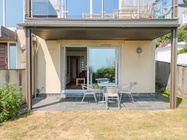 A patio area with a table and four chairs outside sliding glass doors at Rock Pool in Downderry