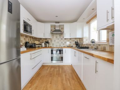 A kitchen with white cabinets wooden countertops stainless steel appliances and tiled backsplash at Rock Pool in Downderry