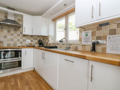 A kitchen with white cabinets wooden countertops a stainless steel oven and range hood and a window with blinds at Rock Pool in Downderry