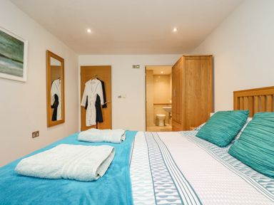 A bedroom with a bed and turquoise pillows a wooden wardrobe and an open door showing a bathroom at Rock Pool in Downderry