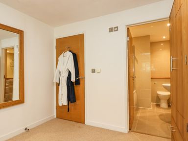A room with a wooden door with bathrobes hanging a large wall mirror and an open door leading to a bathroom at Rock Pool in Downderry