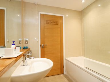 A bathroom with a sink a bathtub a wooden door and toiletries at Rock Pool in Downderry
