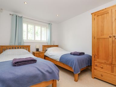 A bedroom with two single beds a wooden wardrobe a window with blue curtains and a bedside table at Rock Pool in Downderry