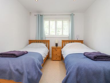 A bedroom with two single wooden beds a small wooden bedside table and a window with blue curtains at Rock Pool in Downderry