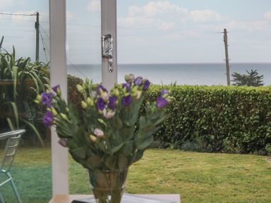 A bouquet of flowers on a table in front of a window showing a garden hedge and the sea beyond at Rock Pool in Downderry