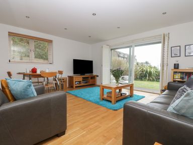 A living room with two sofas a wooden coffee table a TV and a dining table with chairs at Rock Pool in Downderry